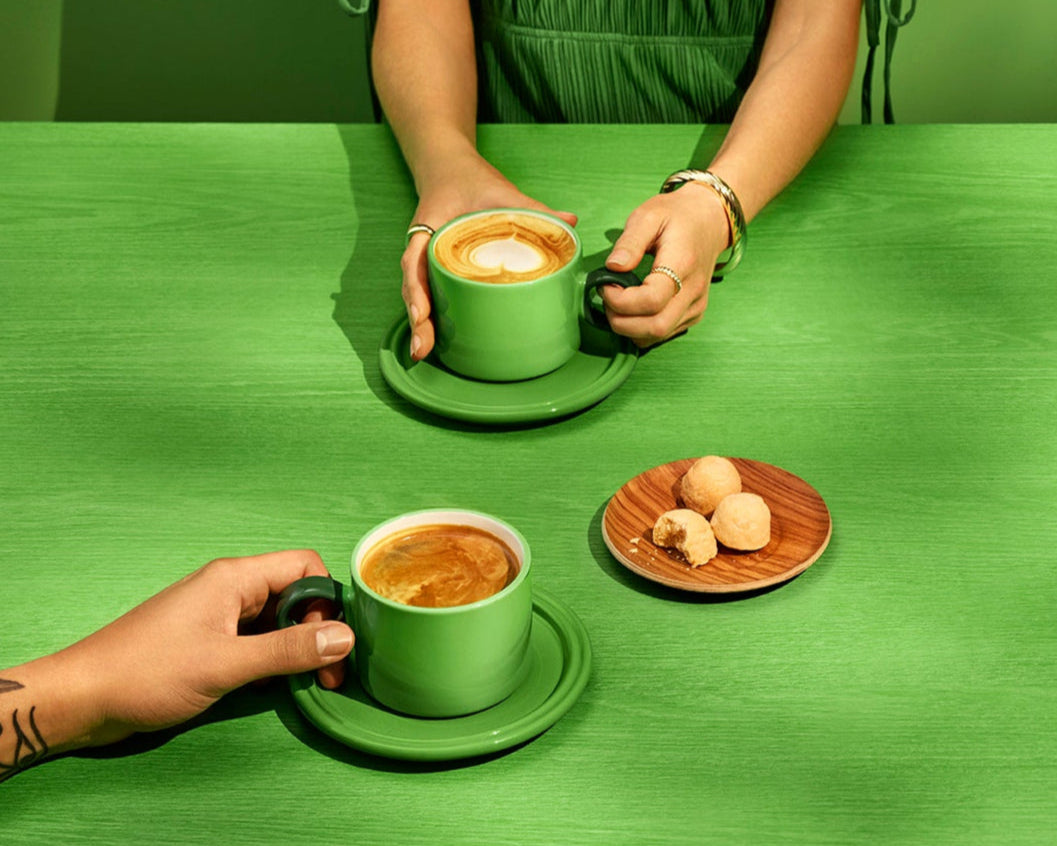 Two people sitting at a green table with green cups and saucers, holding coffee.